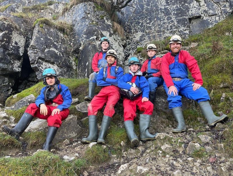 Monmouthshire Caving Group of young people dressed in outdoor gear sitting on a rock.